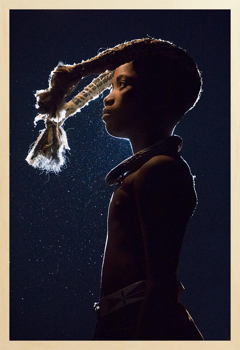 A silhouette of a young Himba girl against the night sky, with a moment of tradition being performed, showing her traditional hair braiding for coming of age.
